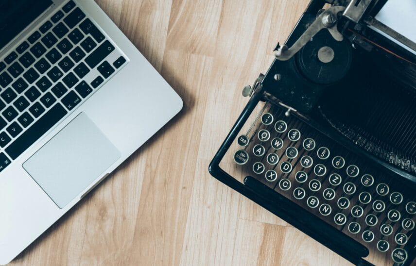 A modern laptop next to a vintage typewriter on a wooden surface.