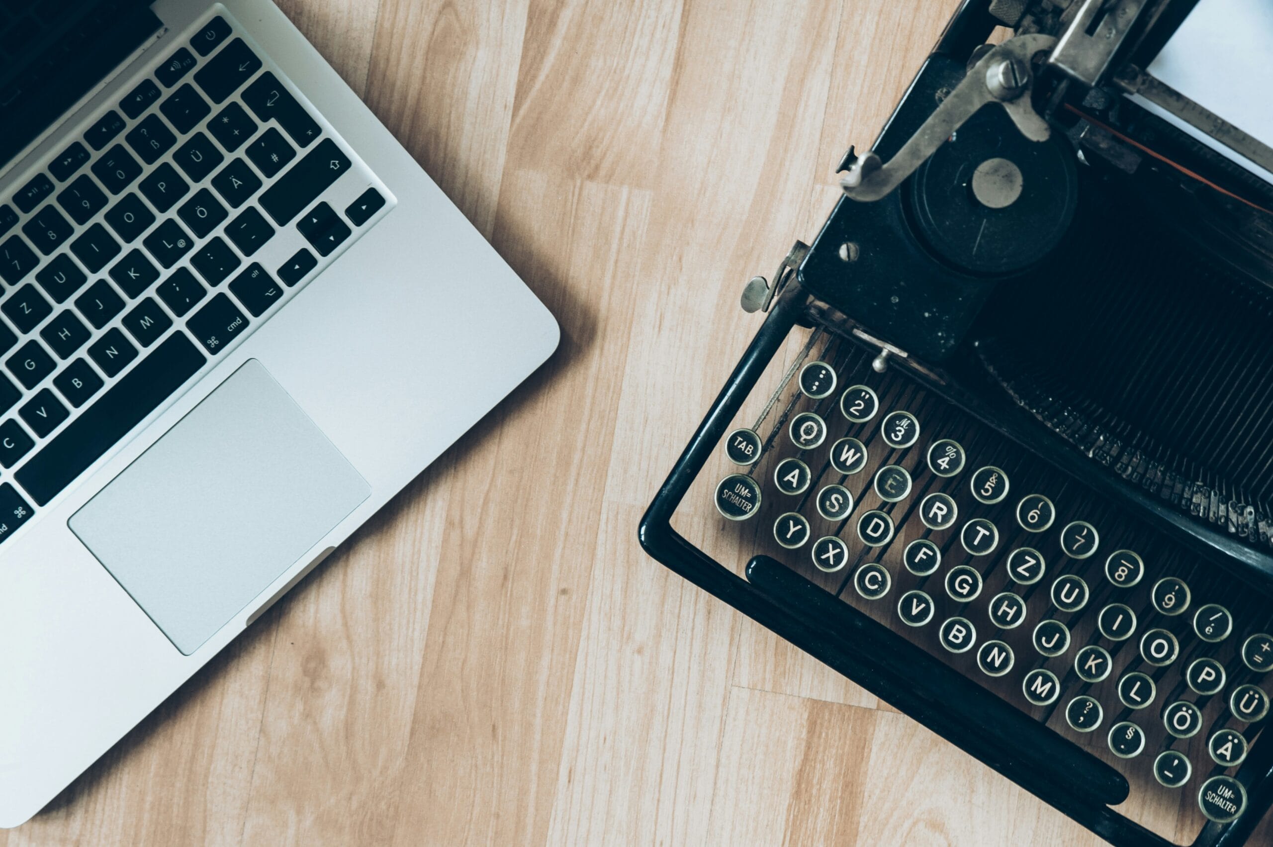 A modern laptop next to a vintage typewriter on a wooden surface.