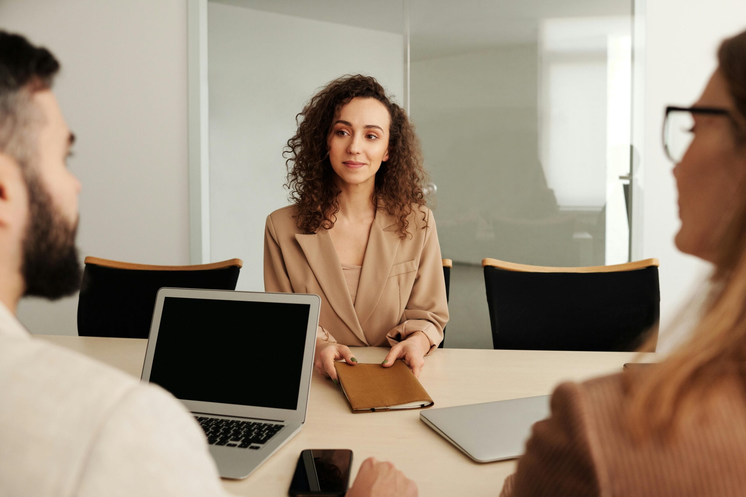 A woman with curly hair sitting at a table during a business meeting, holding a notebook.