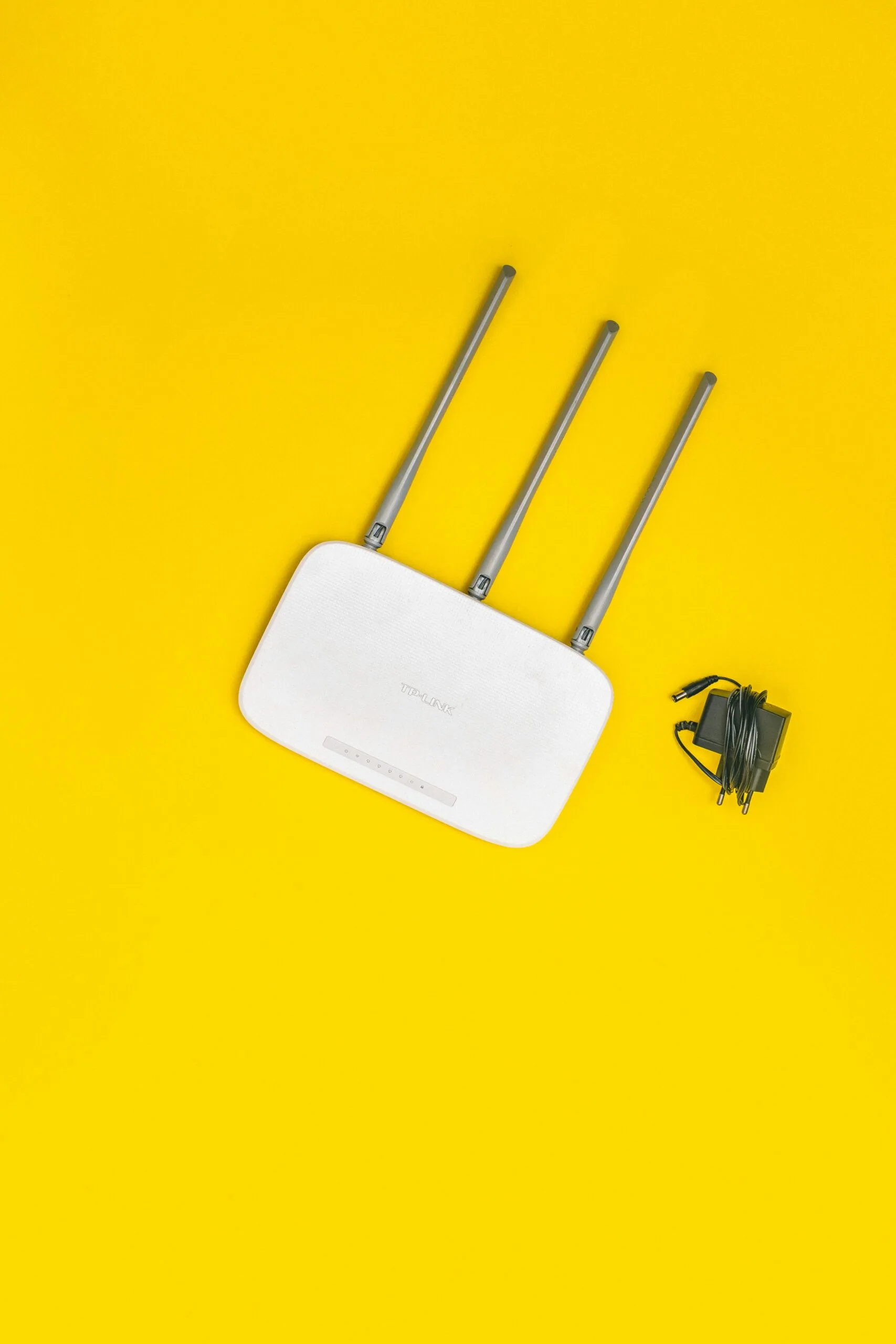 White wireless router with three antennas and power cable on a yellow background.